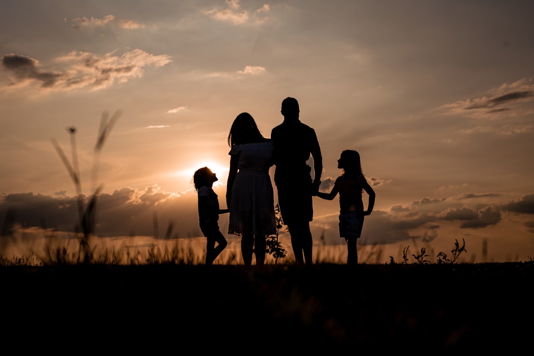 Silhouette of a family of four holding hands at sunset in a grassy field